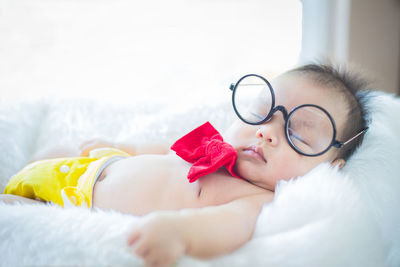 Cute baby boy in eyeglasses lying down on bed