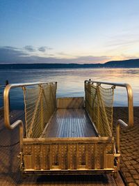 Chairs and table by sea against sky during sunset