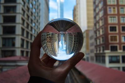 Cropped hand holding crystal ball with reflection in city