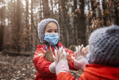 Sibling in red coats wearing respirator masks and medical gloves playing patty cake, social distance