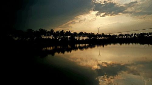 Silhouette trees by lake against sky during sunset