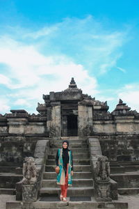 Portrait of woman standing on steps at historic temple against blue sky