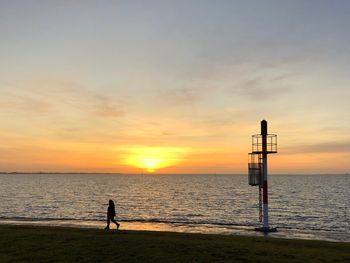 Silhouette person standing on beach against sky during sunset