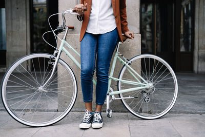 Crop black woman in smart casual style standing along street with bike