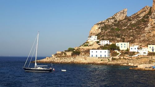 Sailboat on sea by buildings in city against clear sky