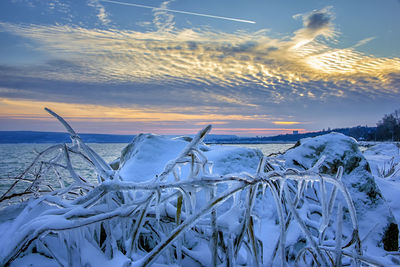 Snow covered land against sky during sunset