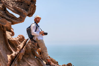 Man with camera on rock formation against sea and sky