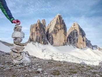 Hiker hand building stony pyramid bellow the three peaks of lavaredo. spring hike in italy alps.