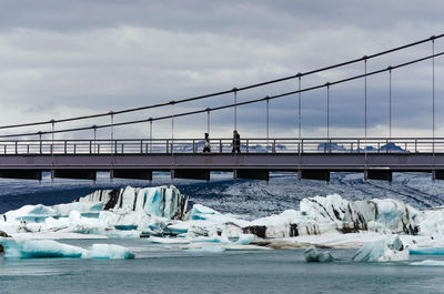 Bridge over frozen lake against sky during winter