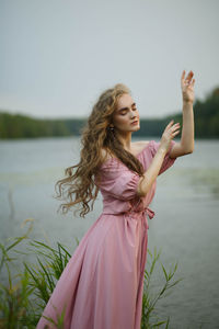 Portrait of young lady in pink dress dancing near the lake