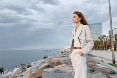 Portrait of young woman standing at beach against sky