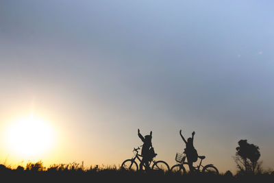 Silhouette people with bicycles on field against clear sky