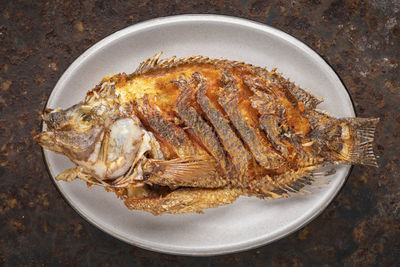 Tasty large fried nile tilapia fish in oval ceramic plate on rusty texture background, top view