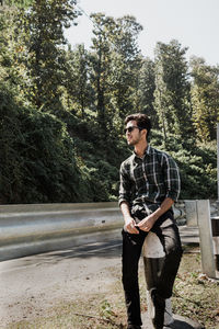 Young man looking away while standing against trees