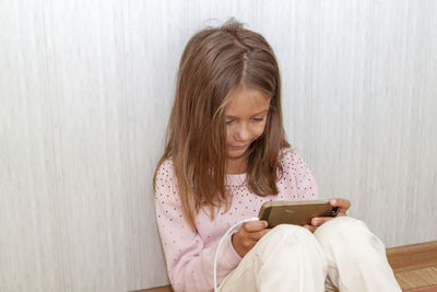 Girl using mobile phone while sitting on wall