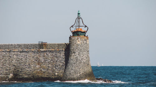 Lighthouse in sea against clear sky