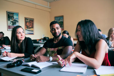 Multi-ethnic friends talking while sitting at desk in classroom