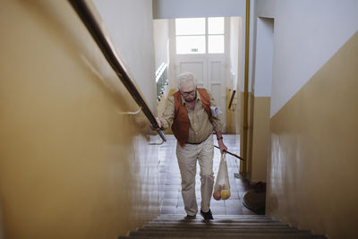 Senior man moving up with bag of fruits on staircase