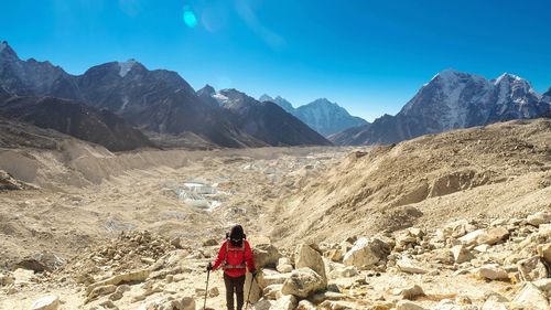 Rear view of person on rock by mountains against sky