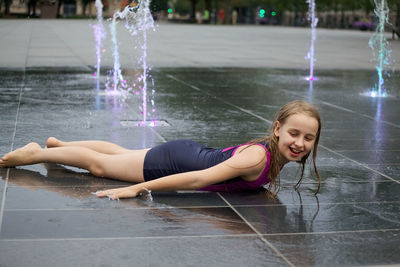 Full length of smiling girl lying on wet street