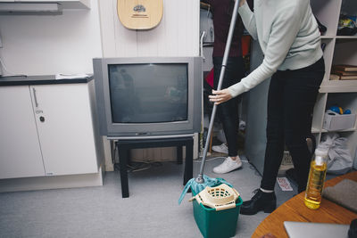 Low section of woman holding mop in bucket at college dorm