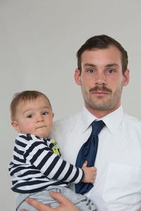 Portrait of father carrying baby boy against white background