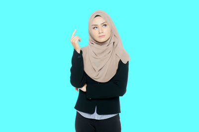 Thoughtful young woman wearing hijab while standing against blue background