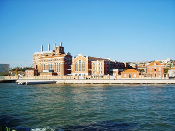 Buildings by sea against clear blue sky