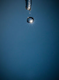 Close-up of droplet falling from icicle against clear blue sky