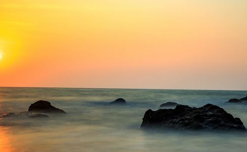 Rocks in sea against sky during sunset