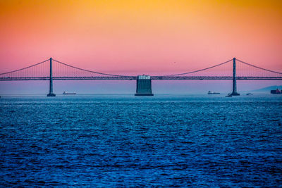 View of suspension bridge over river against clear orange sky