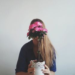 Woman holding flower against wall at home