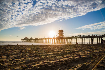 Pier on sea and beach against sky during sunset