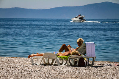 Rear view of couple sitting on chair by sea against sky