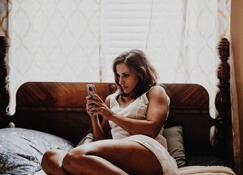 Beautiful woman reclining on bed while using mobile phone at home