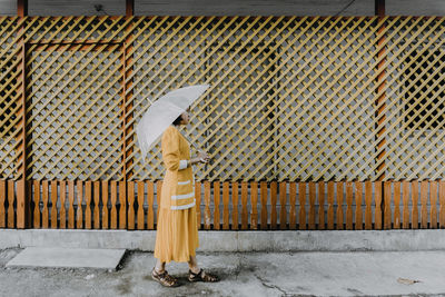 Side view of woman with umbrella walking on footpath by house