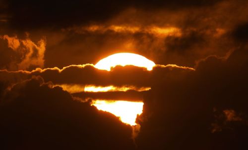 Low angle view of sun shining through clouds during sunset