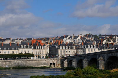 Bridge over river by buildings in city against sky
