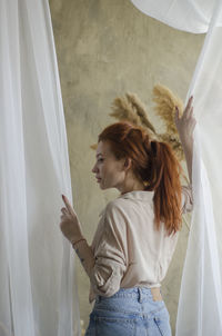 Side view of woman standing against white curtain