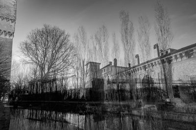 Reflection of bare trees in water against sky