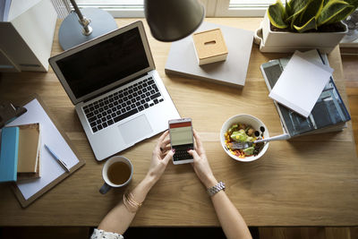 Overhead view of woman using smart phone at desk in home office