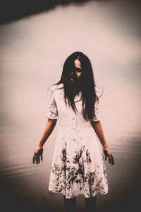 Woman standing in sea against sky during sunset