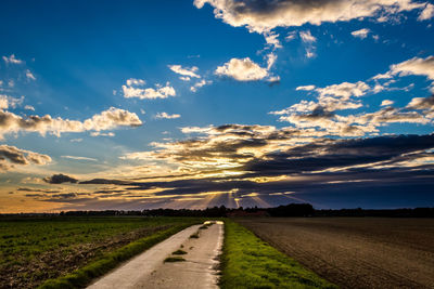 Empty road amidst field against sky during sunset