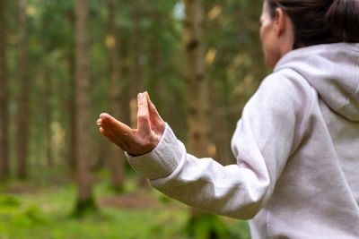 Cropped unrecognizable female traveler sitting on tree stump in lotus pose and doing yoga with closed eyes while enjoying woods