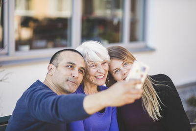 Multi-generation family smiling while taking selfie outside nursing home