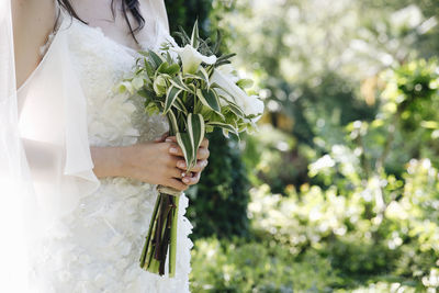 Midsection of bride holding white flowers at park