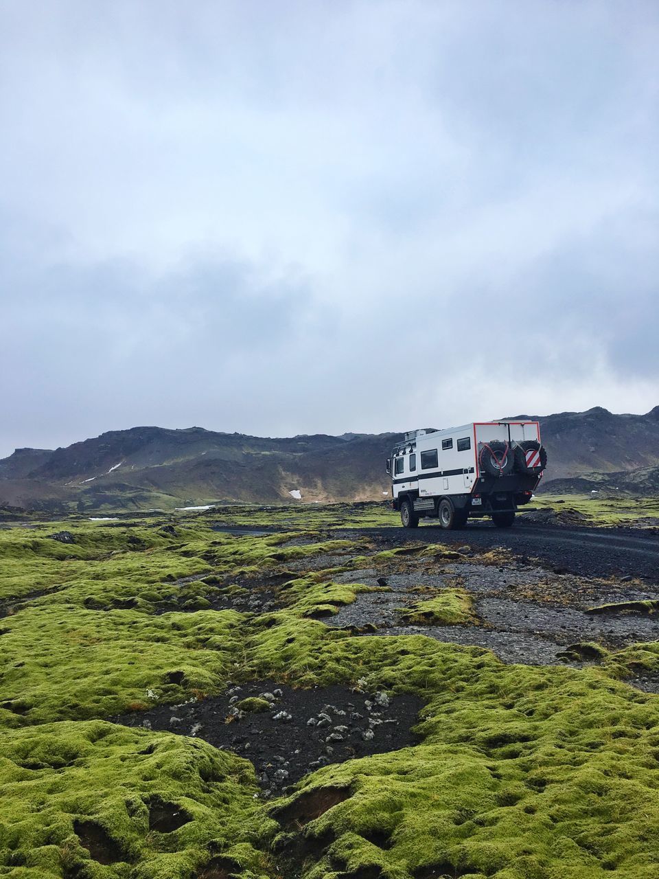 transportation, mode of transport, land vehicle, sky, landscape, car, mountain, green color, cloud - sky, travel, field, nature, grass, day, tranquil scene, on the move, scenics, beauty in nature, journey, non-urban scene