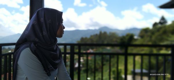 Side view of man looking at railing against trees