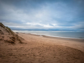 Scenic view of beach against cloudy sky