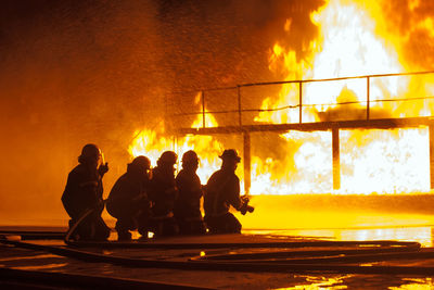 Silhouette firefighters spraying water on fire at night